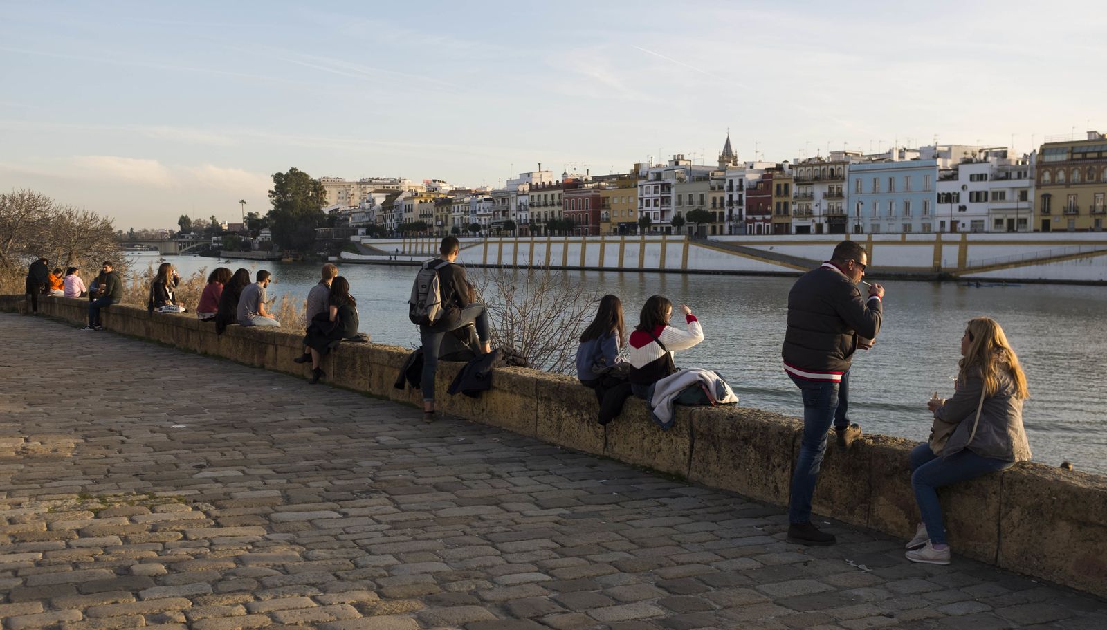Varios jóvenes disfrutan del sol en una de las orillas del río en Sevilla.