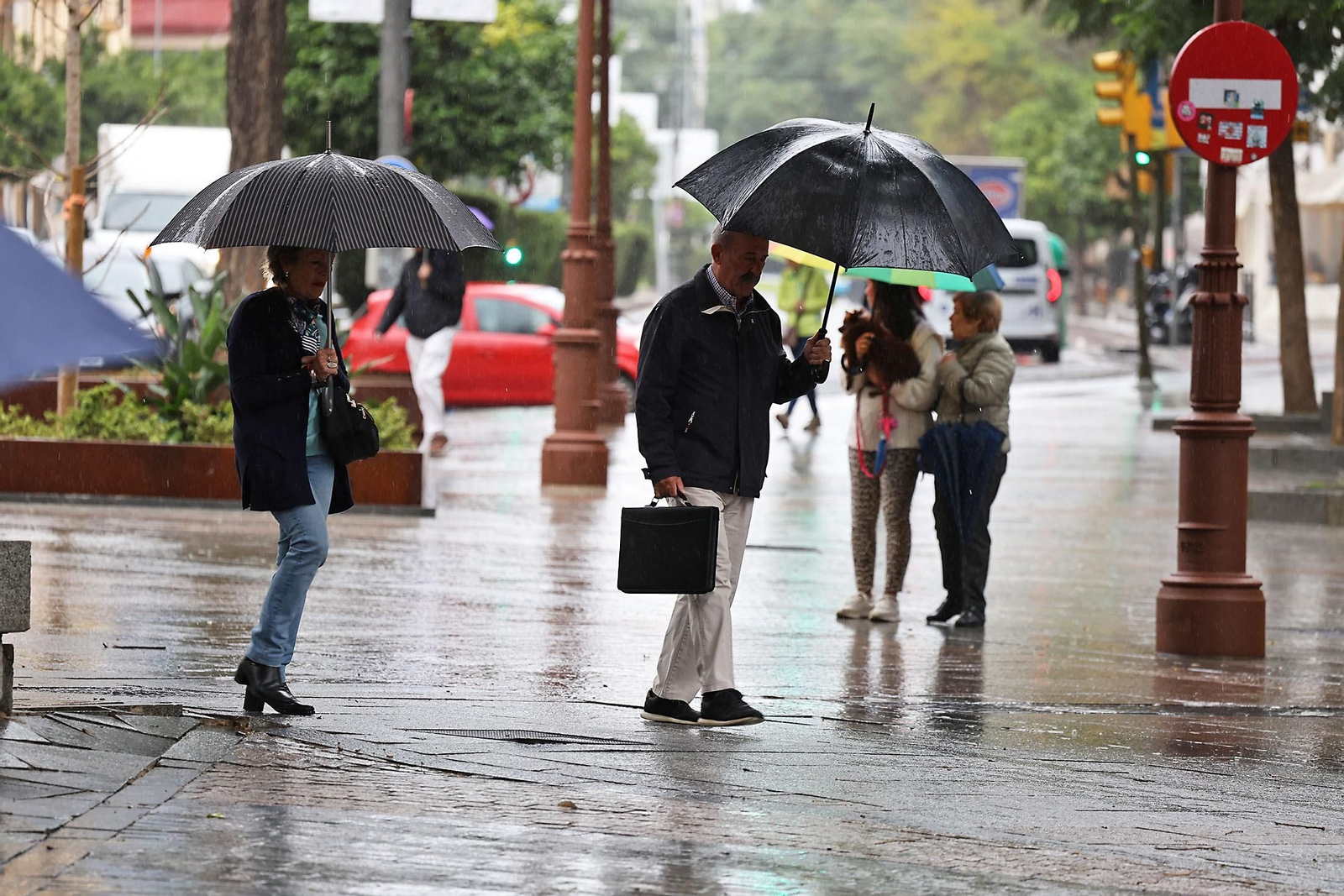 Varias personas se protegen de la lluvia con paraguas en el centro de Huelva.