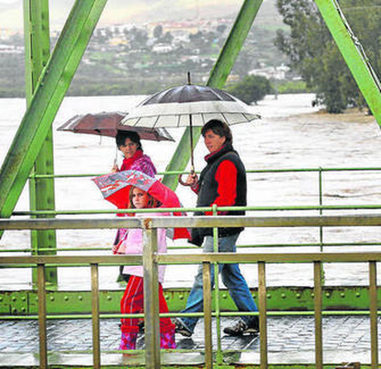 Una familia pasea bajo la lluvia en el puente de la Estación de Cártama.