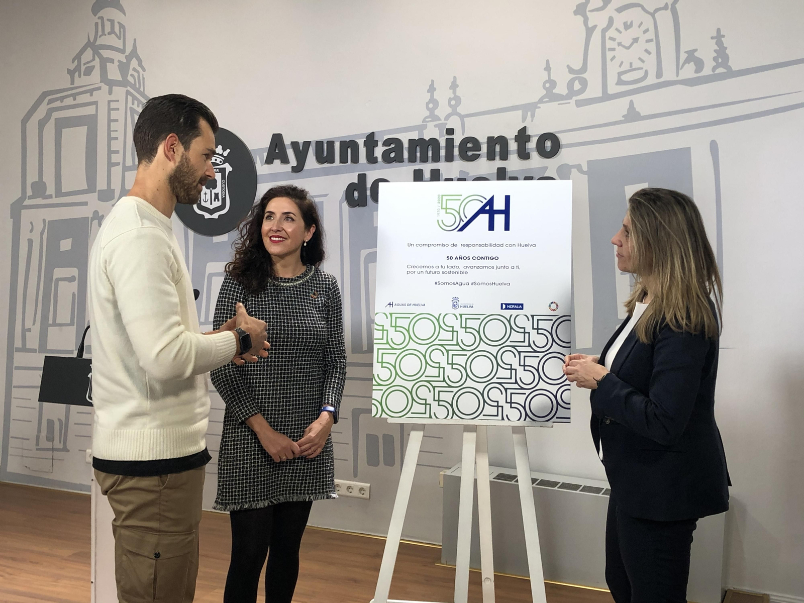 El diseñador Rafael Fuentes explica los detalles del logo a la gerente de la empresa, Isabel Butrón, y a la teniente de alcalde María Villadeamigo.