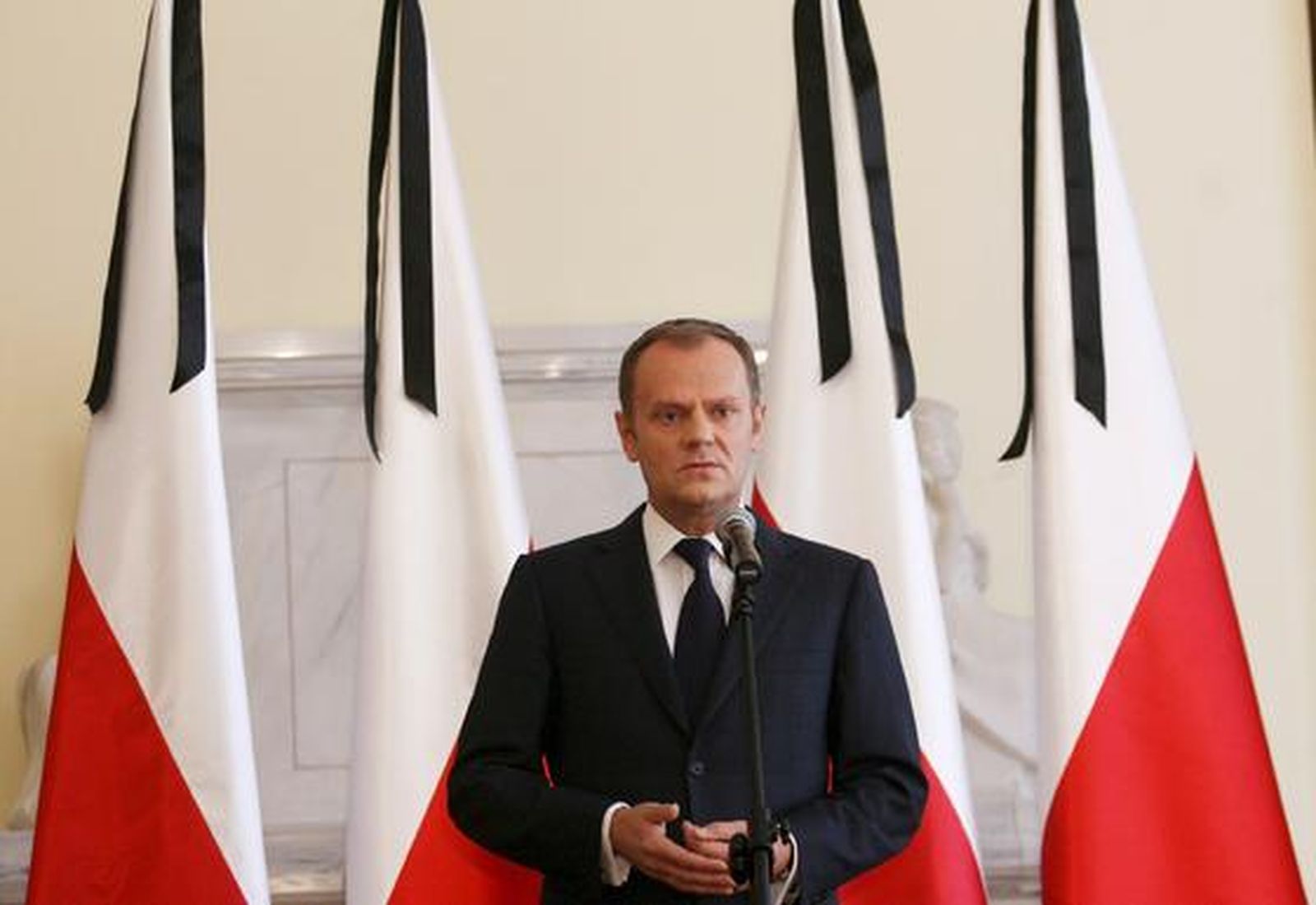 El primer ministro polaco, Donald Tusk, comparece ante los medios rodeado de banderas con crespones negros. / EFE