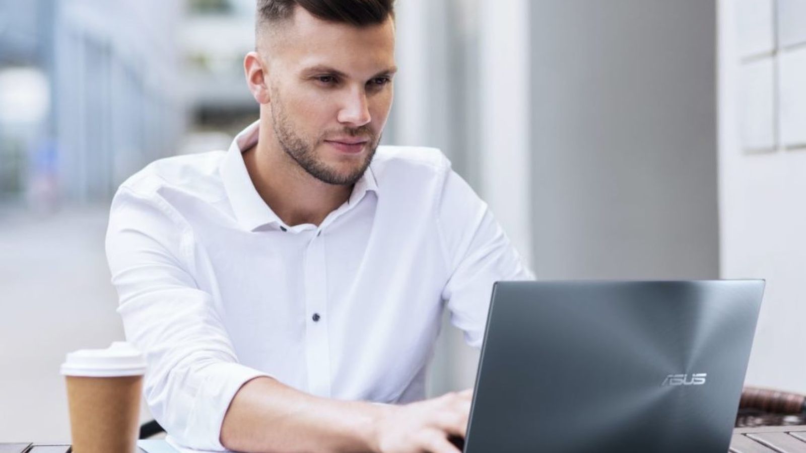 Un joven usando el ordenador portátil mientras toma un café