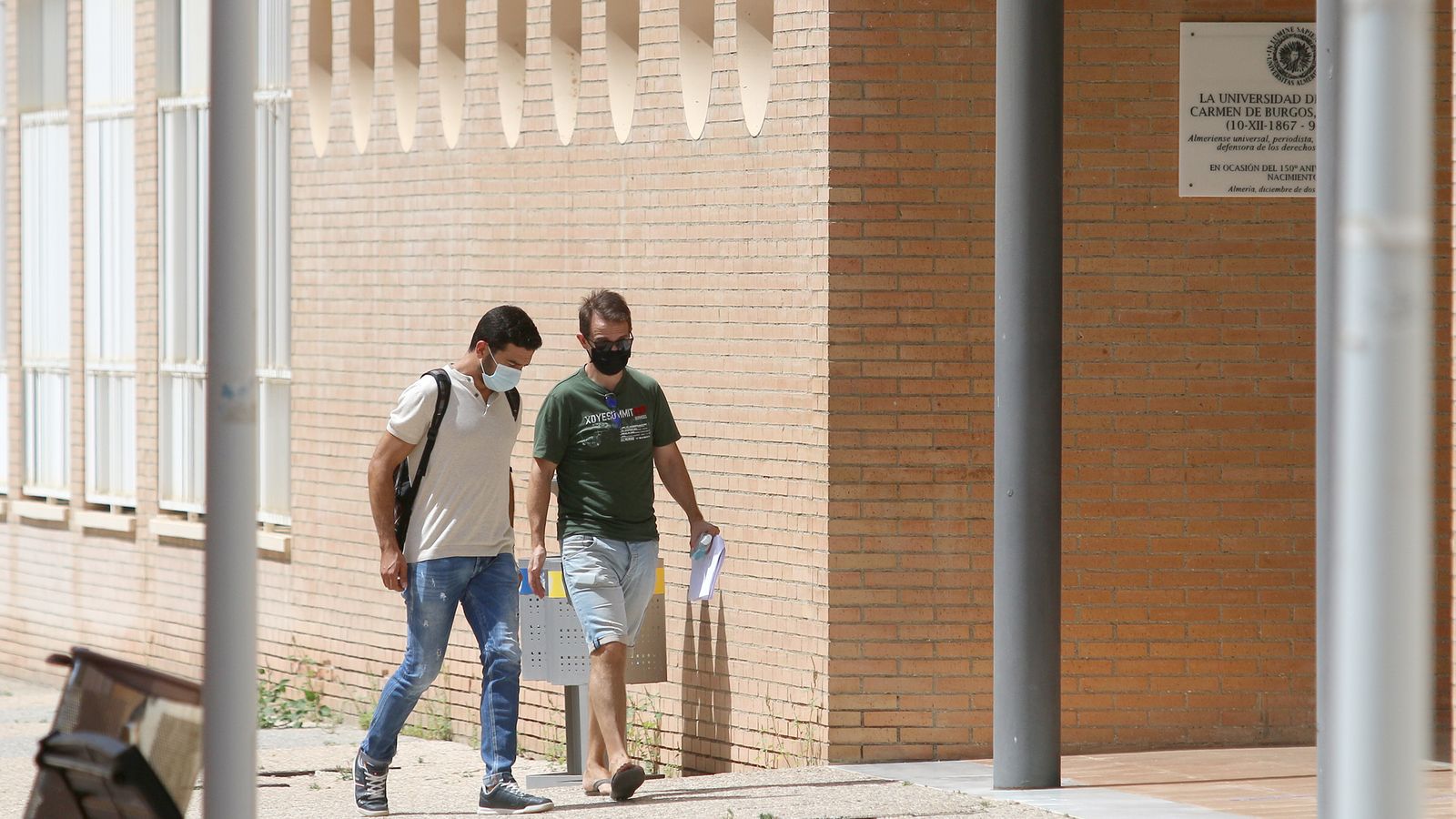 Dos chicos caminan con mascarilla por el campus universitario