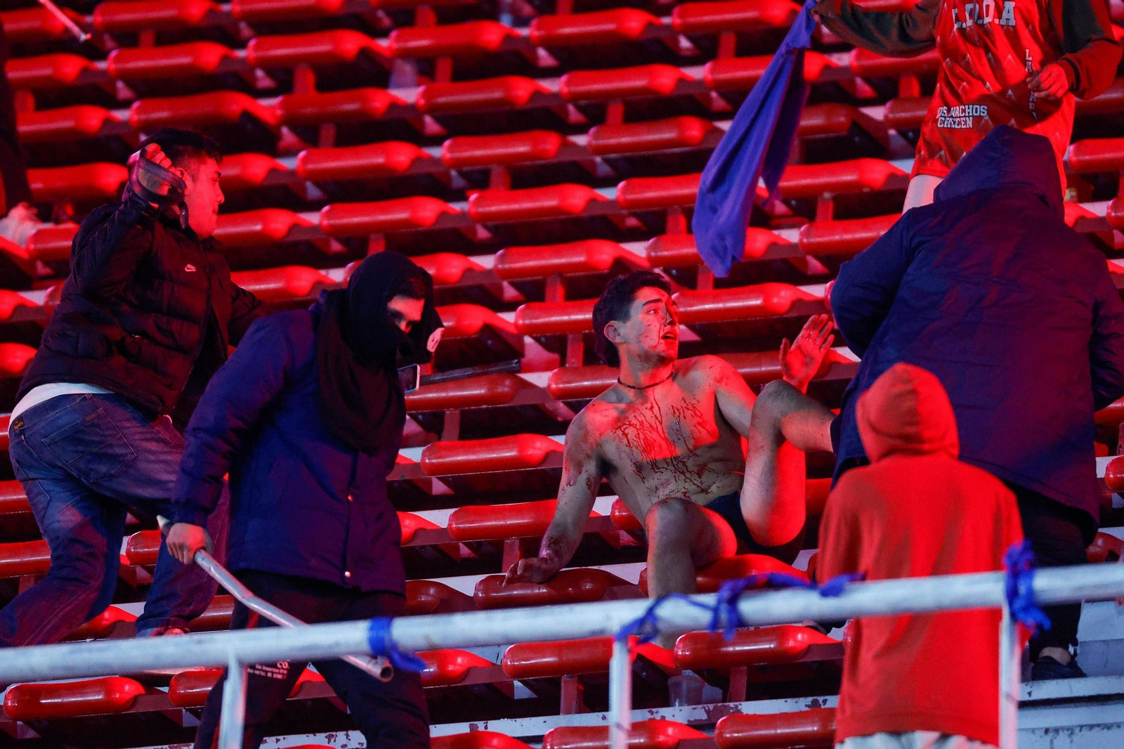 Un hincha ensangrentado es apaleado por otros aficionados en las gradas.