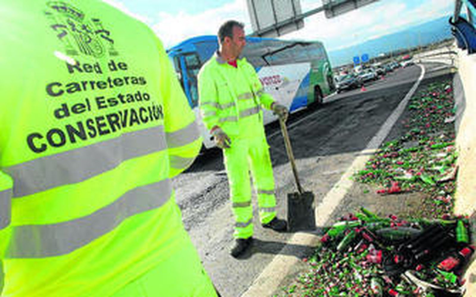 Dos operarios de Conservación de Carreteras recogen los restos de cristales con las colas de vehículos, ayer.