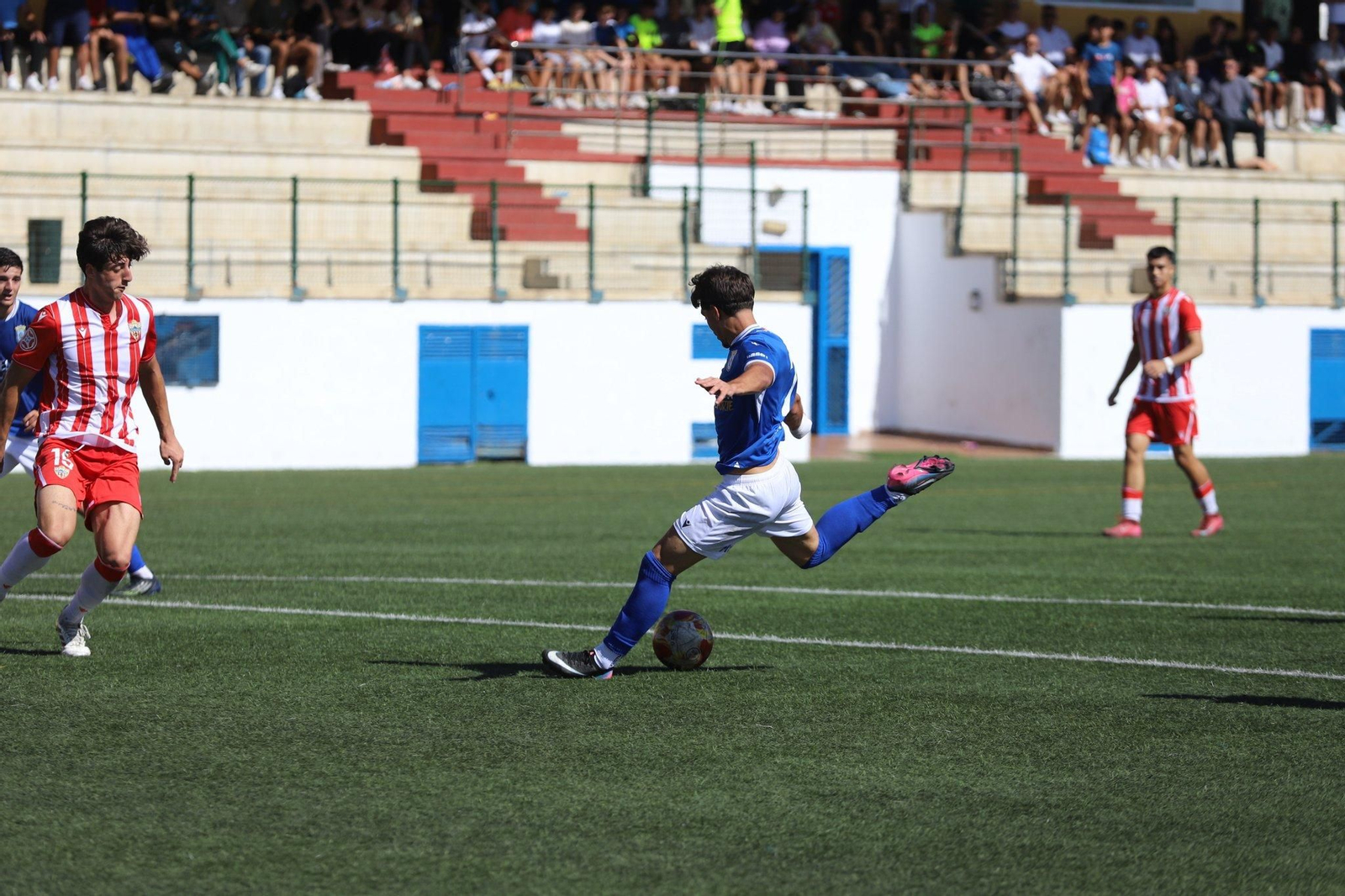 Un jugador melillense prepara la pierna para el disparo ante la aparición del rojiblanco Diego Sánchez.