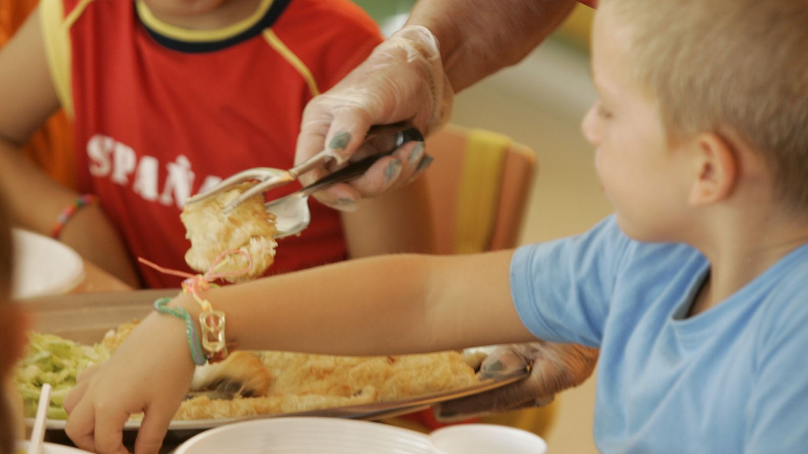 Una monitora de comedor sirve el pescado a los niños.