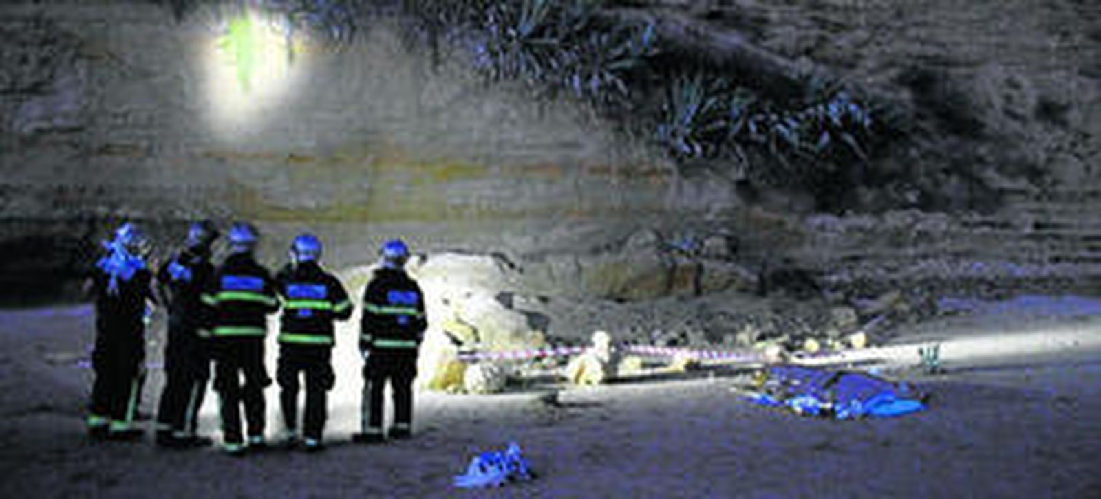 Un grupo de bomberos inspecciona a última hora de la tarde de ayer el lugar del desprendimiento, con el cadáver tapado a la derecha.
