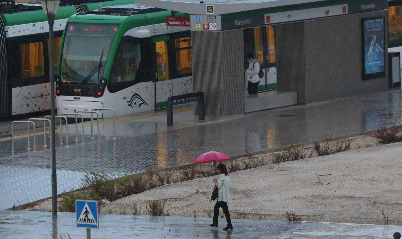 Una mujer, con paraguas, se dirige a una de las estaciones del Metro de Málaga en superficie.
