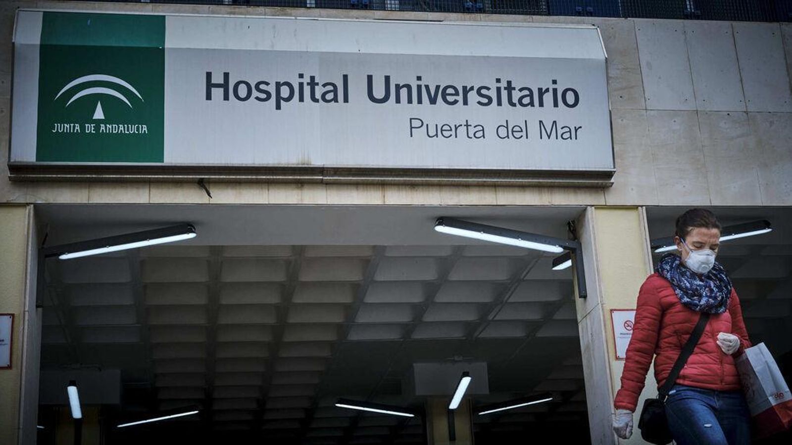 Una mujer con mascarilla y guantes saliendo del  Puerta del Mar.