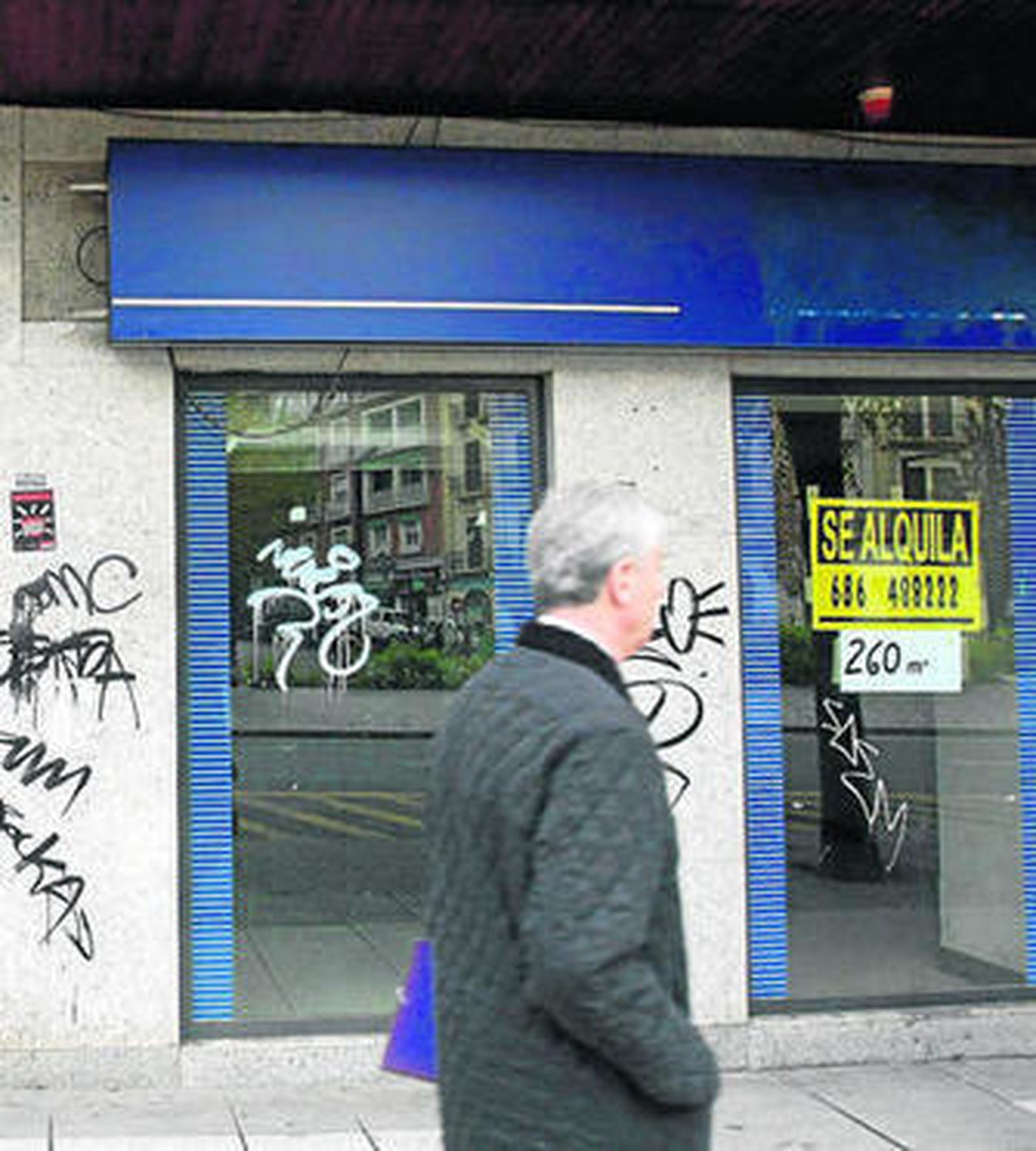 Un señor pasa junto a una oficina cerrada de una entidad bancaria.
