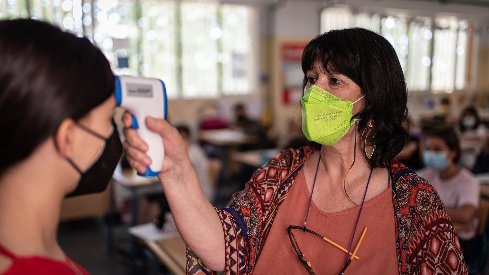 Una maestra toma la temperatura a una de sus alumnas.