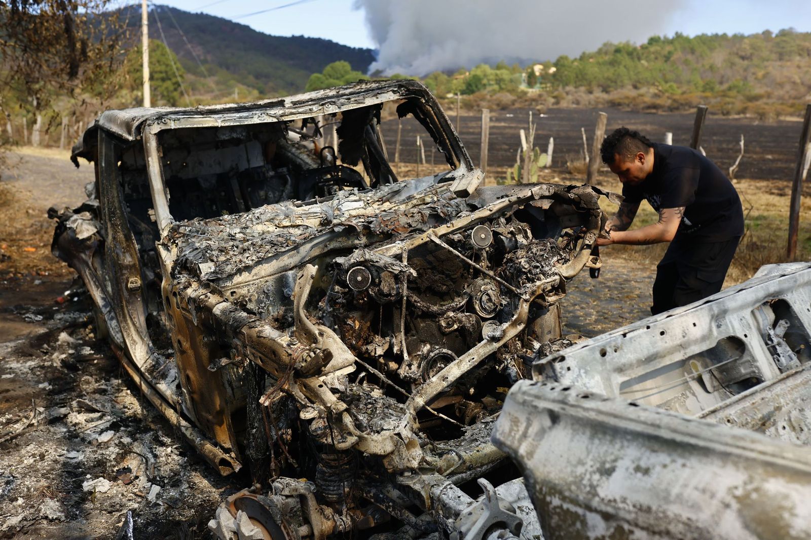 Una persona toma una fotografía a un vehículo incinerado frente a la entrada del Hotel Tapalpa Country Club este miércoles, en Tapalpa (México ).