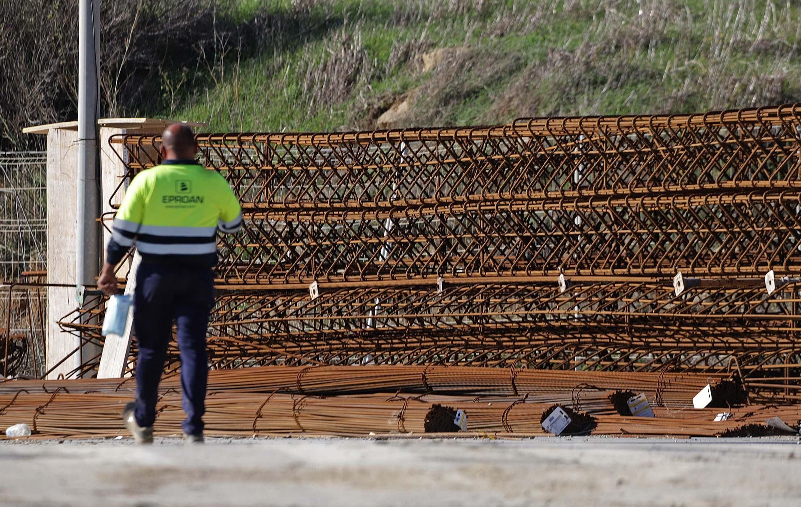Un trabajador de la construcción camina junto a gavillas de acero para encofrados en una obra en Algeciras.