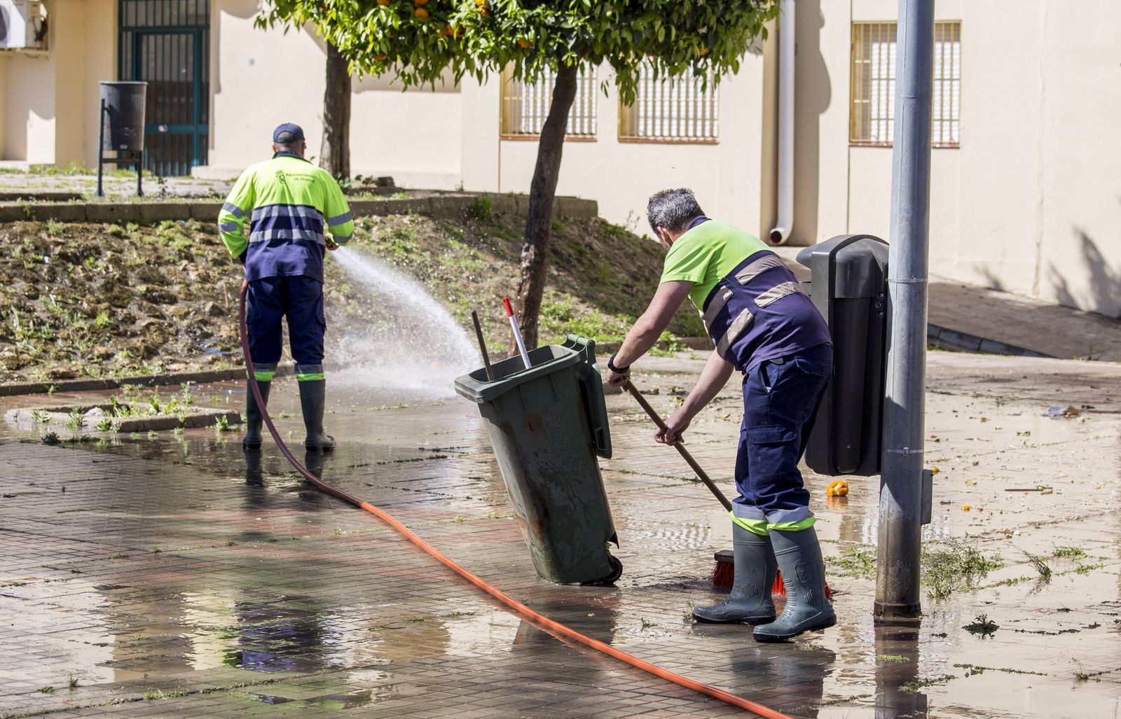 Dos operarios del servicio municipal limpian con mangueras un espacio público de la capital onubense.