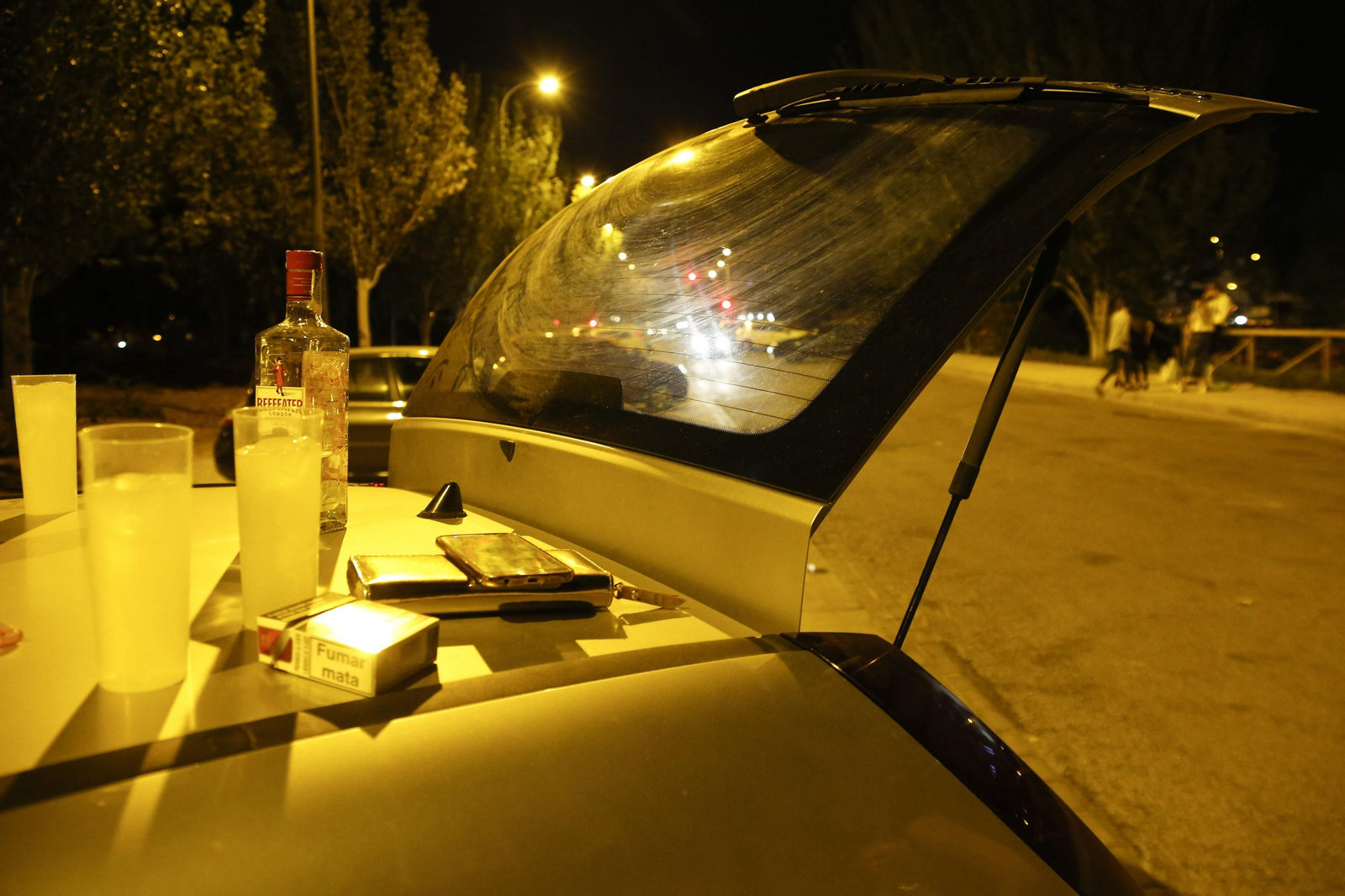 Jóvenes durante un botellón dejan las bebidas sobre un vehículo.