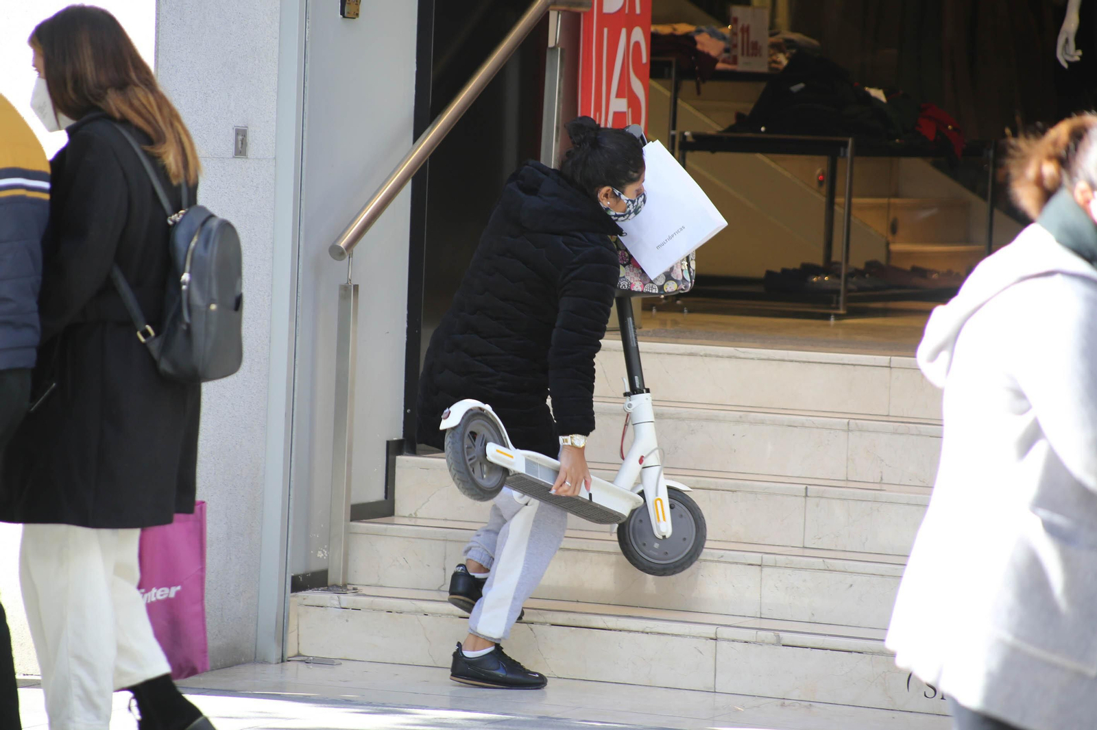 Una mujer, accediendo a una tienda con su patinete eléctrico. Una mujer, accediendo a una tienda con su patinete eléctrico.