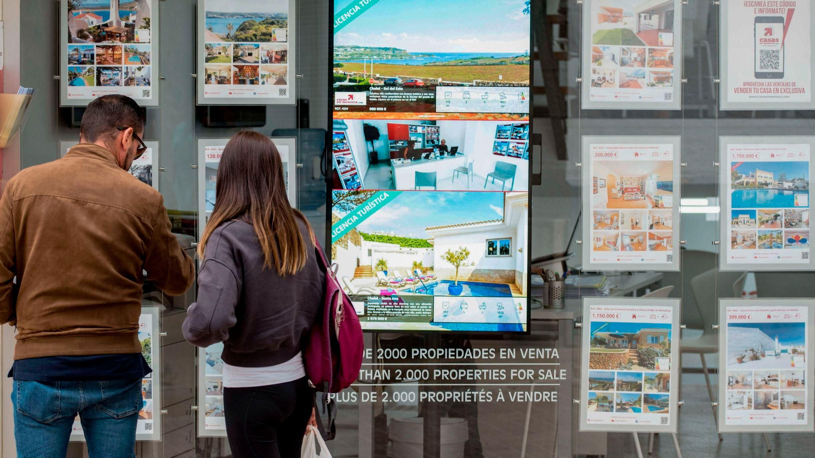 Una pareja se detiene a observar las ventas de viviendas  anunciadas en una inmobiliaria.