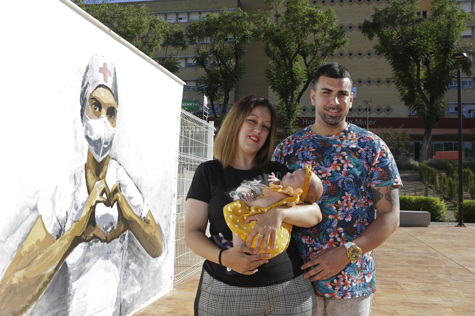 Miriam junto a su pareja y la pequeña Suhaila junto al mural en Homenaje a la Enfermería en el Hospital de la Mujer.