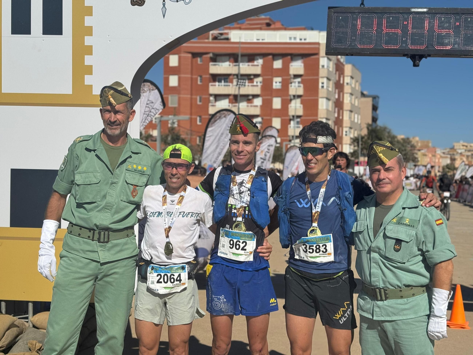 Los marchadores ganadores de esta edición de La Desértica posan con sus medallas junto a la línea de meta.