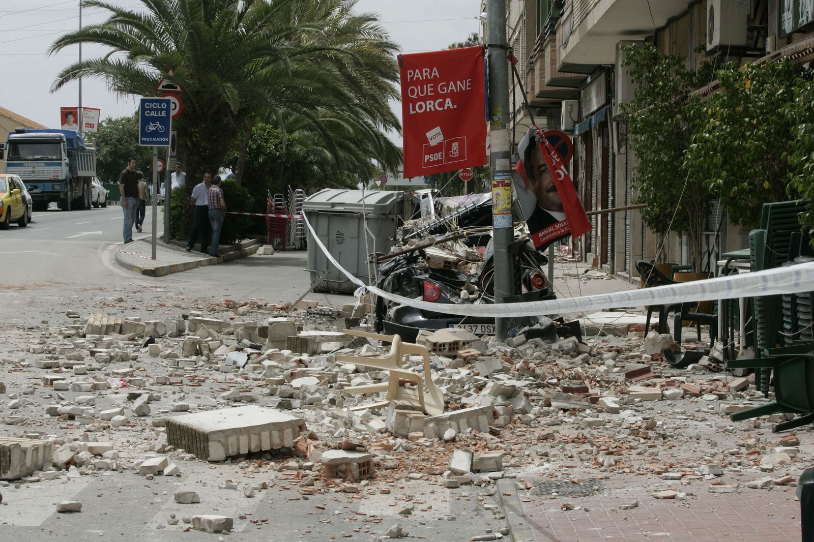 Escombros de una fachada derrumbada cubren la calzada y aplastan un vehículo en una calle de Lorca, acordonada tras un seísmo que provoca importantes daños materiales.