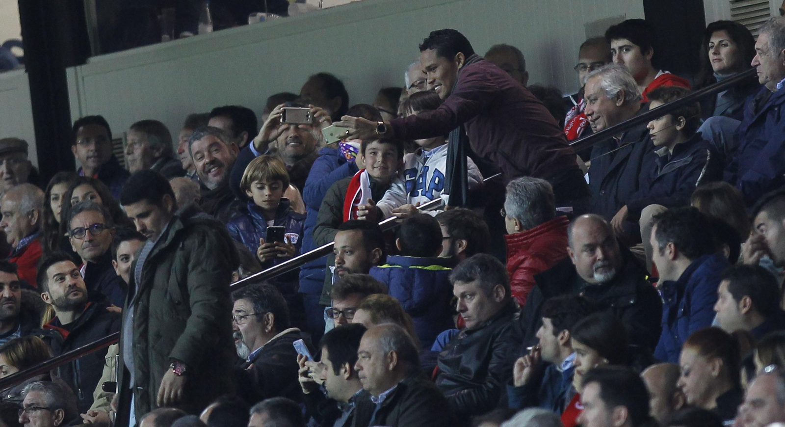 Carlos Bacca se hace una foto con unos jóvenes aficionados en el palco del Sánchez-Pizjuán, ante Javier Arenas.
