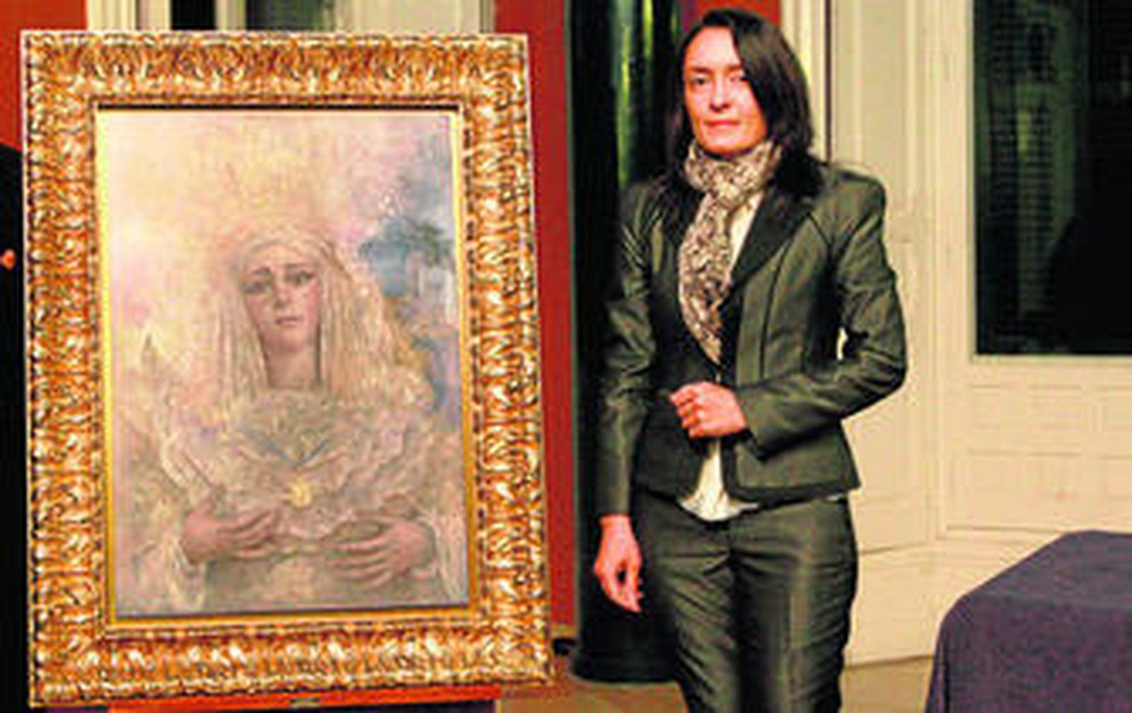 La pintora sevillana Isabel Sola posa junto a su obra que ilustrará el cartel oficial de la Coronación de la Virgen de la Victoria.
