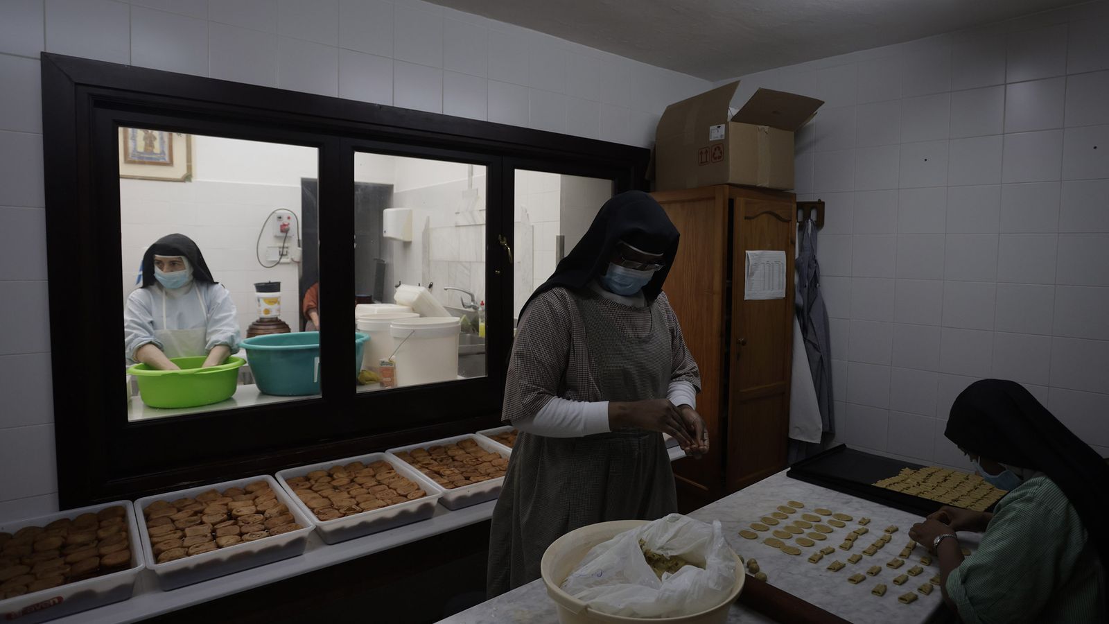 Dos religiosas trabajan en el obrador frente a las fuentes de torrijas ya preparadas.