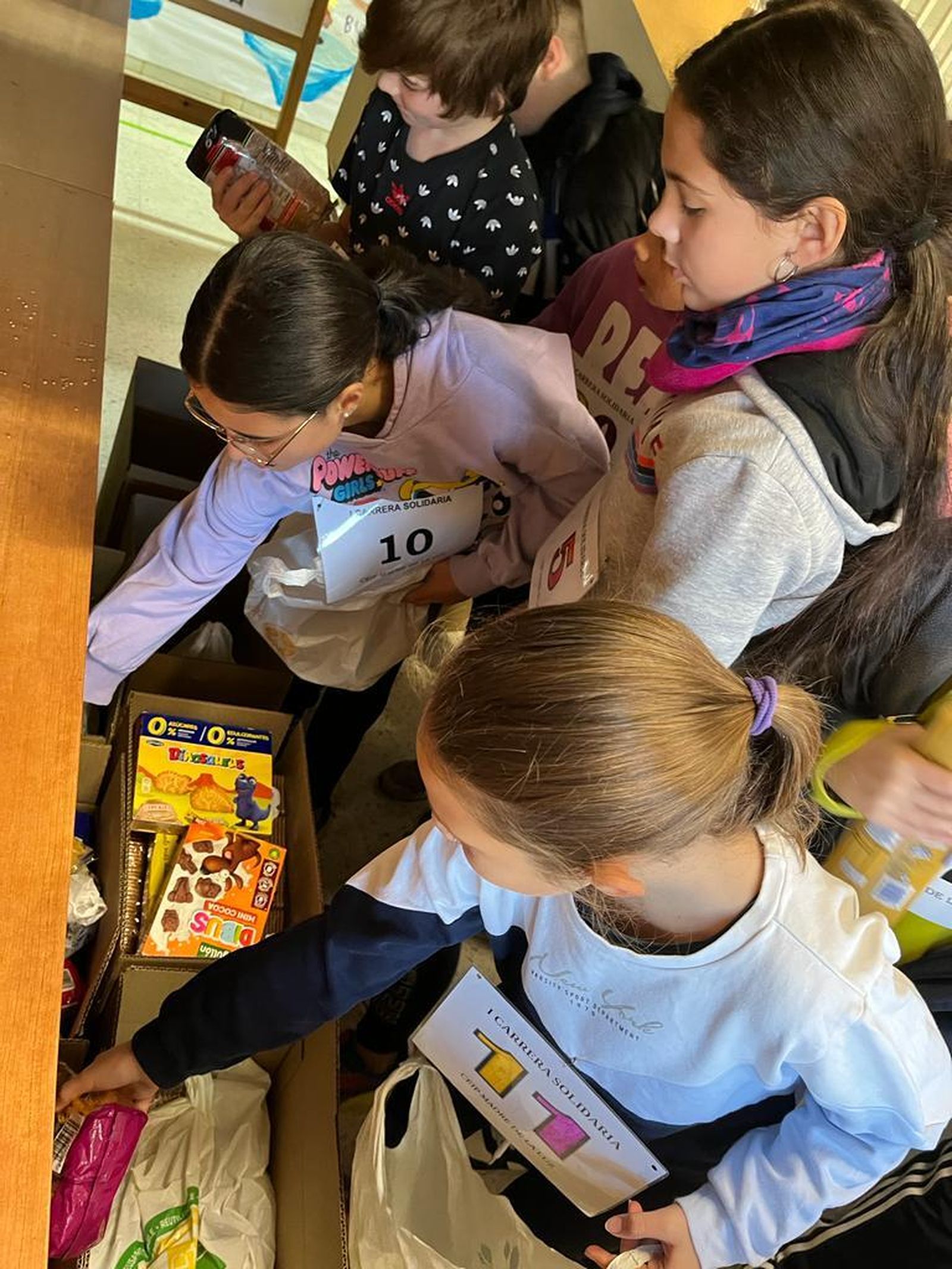 Los alumnos con los dorsales dejando su aportación de alimentos en cajas.