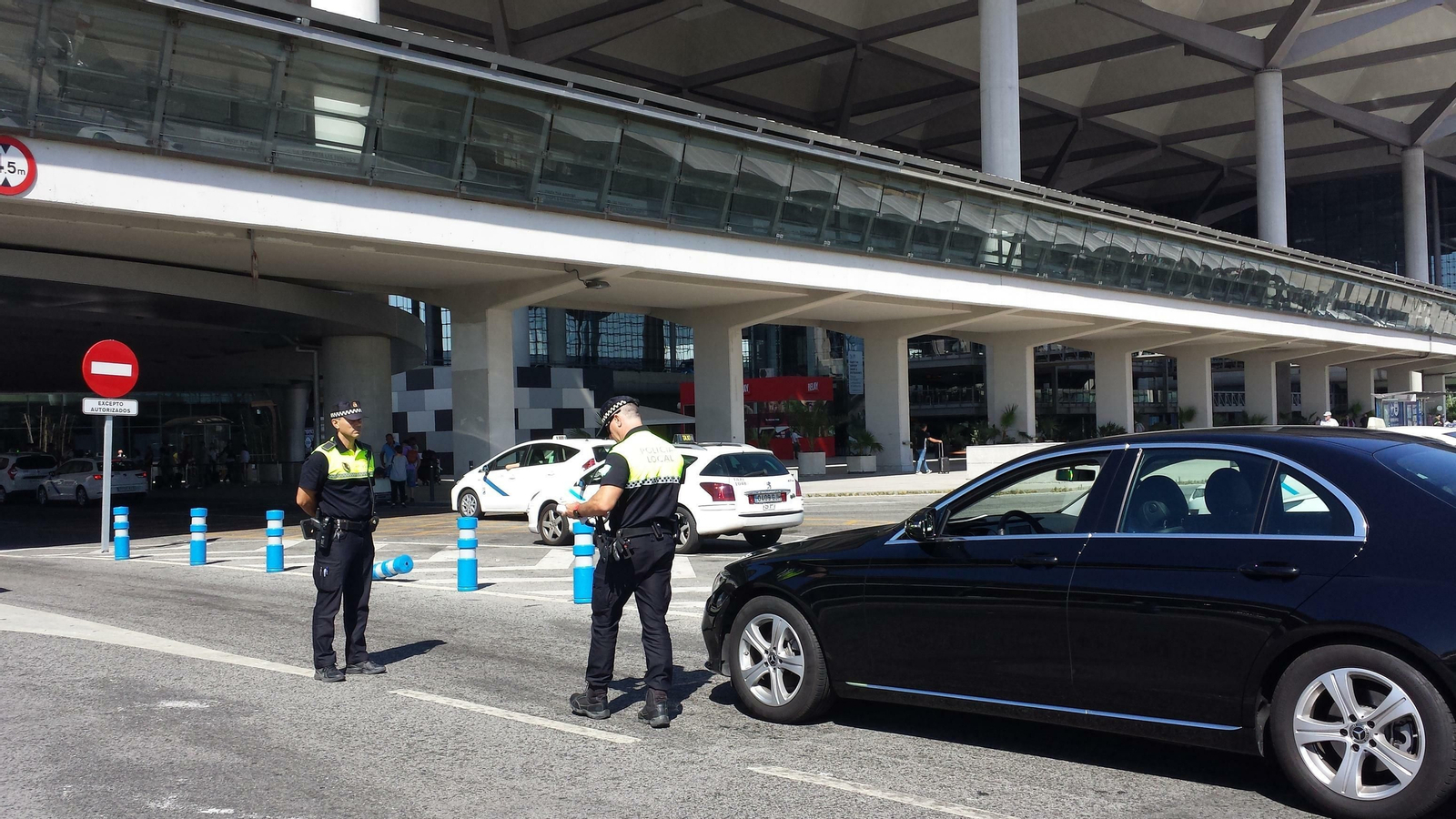 Dos policías locales observan un VTC parado en el aeropuerto de Málaga junto a una parada de taxis.