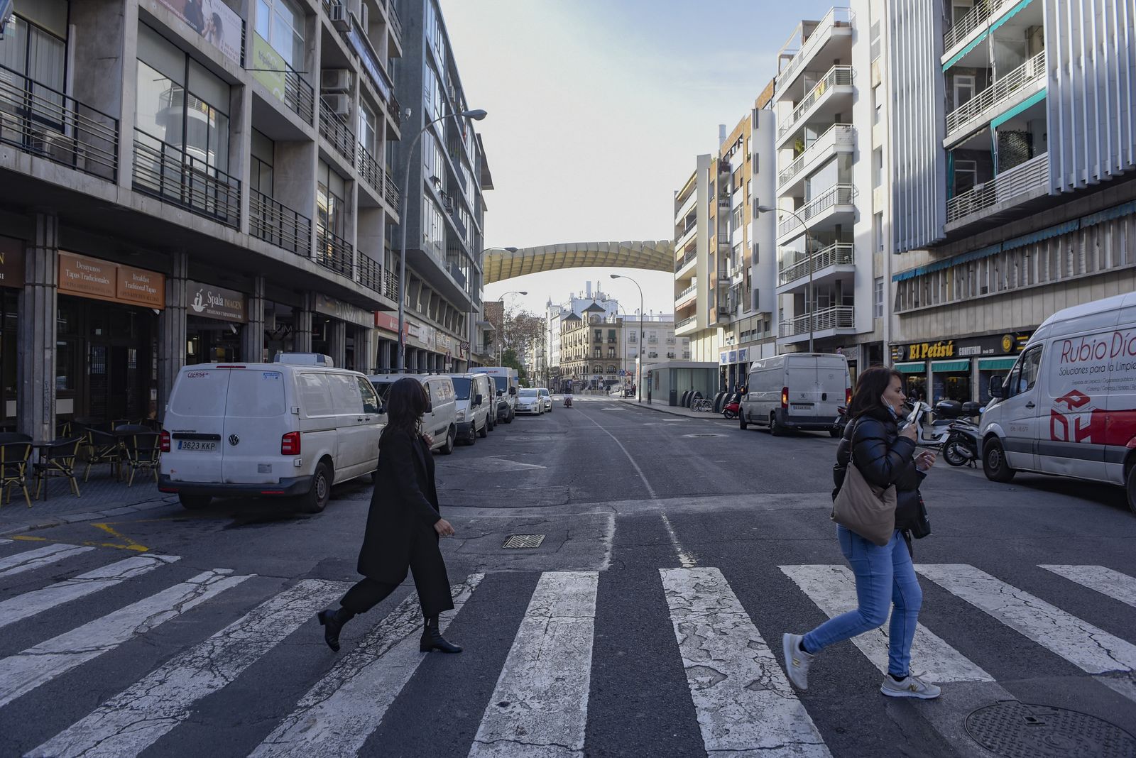 Dos mujeres cruzan un paso de peatones en una calle Imagen repleta de vehículos en carga y descarga.