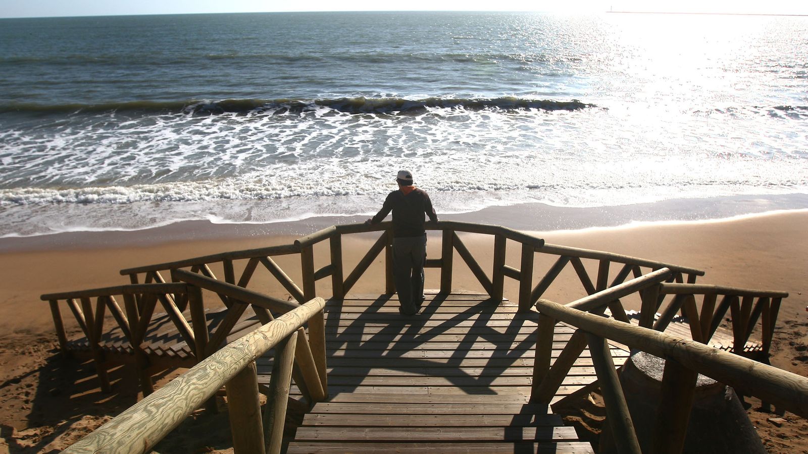 Un veraneante se asoma a una de las pasarelas de acceso a una playa de la Costa onubense.
