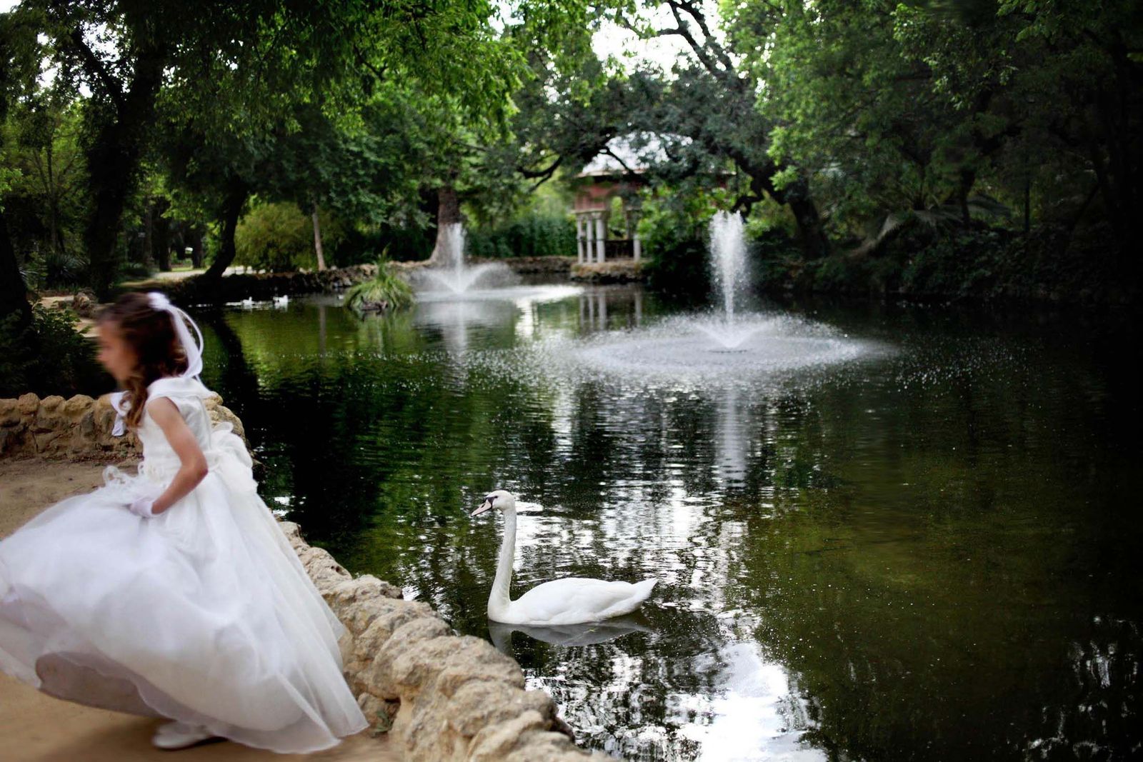 Una niña vestida de primera comunión posa en un estanque del Parque de María Luisa.