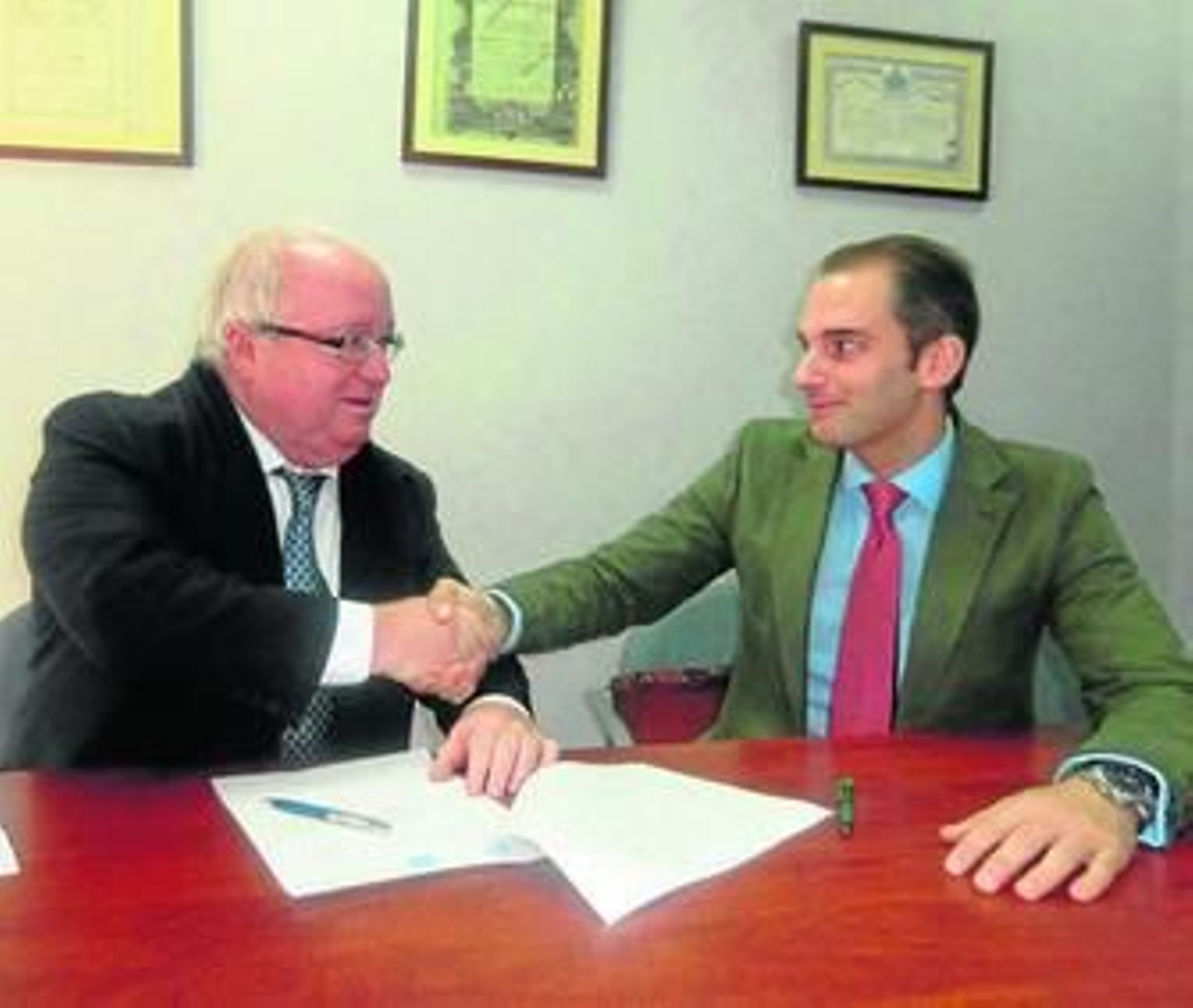 Carlos Medina (i), como apoderado de la empresa, estrecha la mano al notario Carlos Cabrera tras la firma de los documentos.