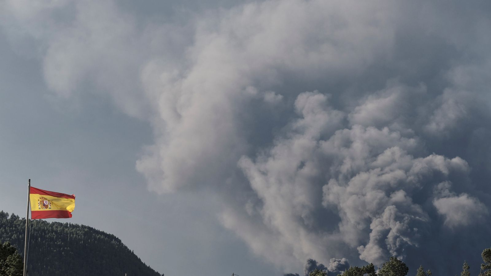El fuerte viento imperante a primera hora de este jueves, hace ondear la bandera española ubicada en el Puesto de Mando Avanzado (PMA) con el volcán de La Palma de fondo.