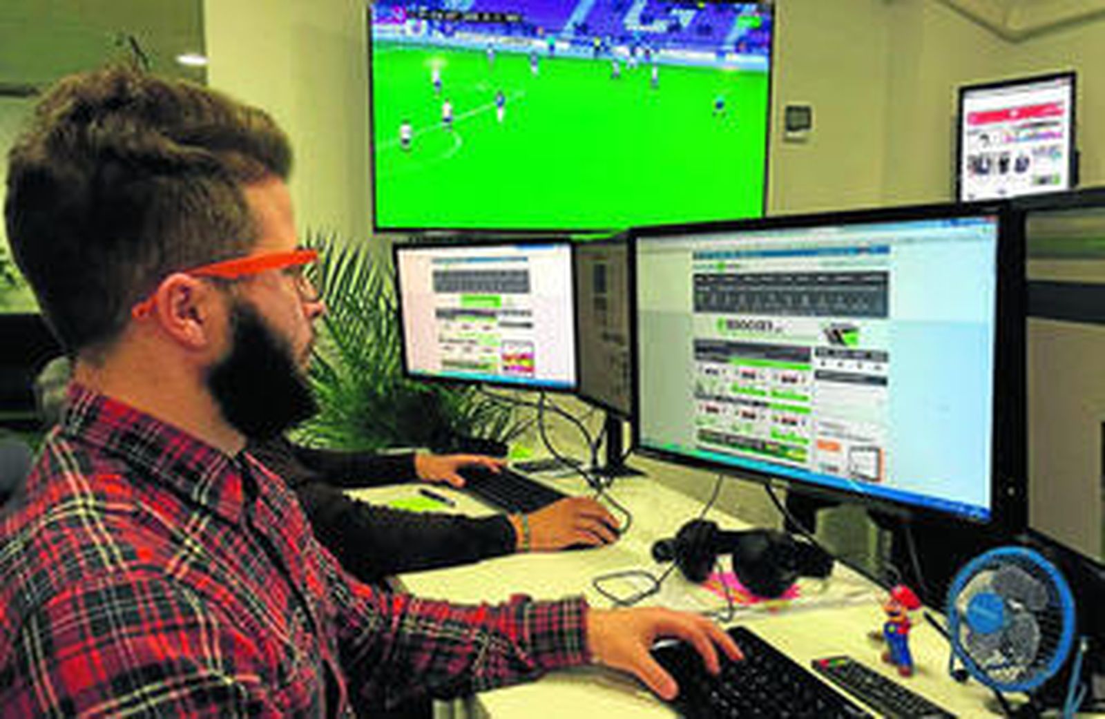 Un empleado trabaja en la plataforma con un partido de fútbol en el televisor de fondo.