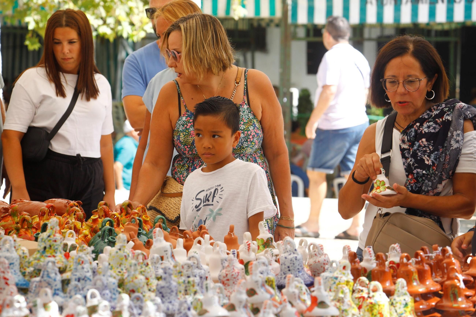 Un grupo de personas, junto a un puesto de las tradicionales campanitas de la Velá