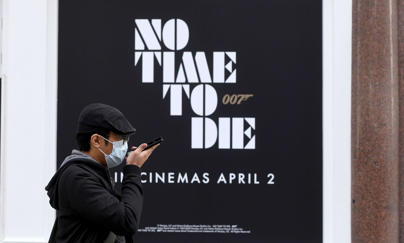 Un ciudadano con mascarilla, en Londres, ante un cartel con la antigua fecha de estreno de 'No Time To Die'.