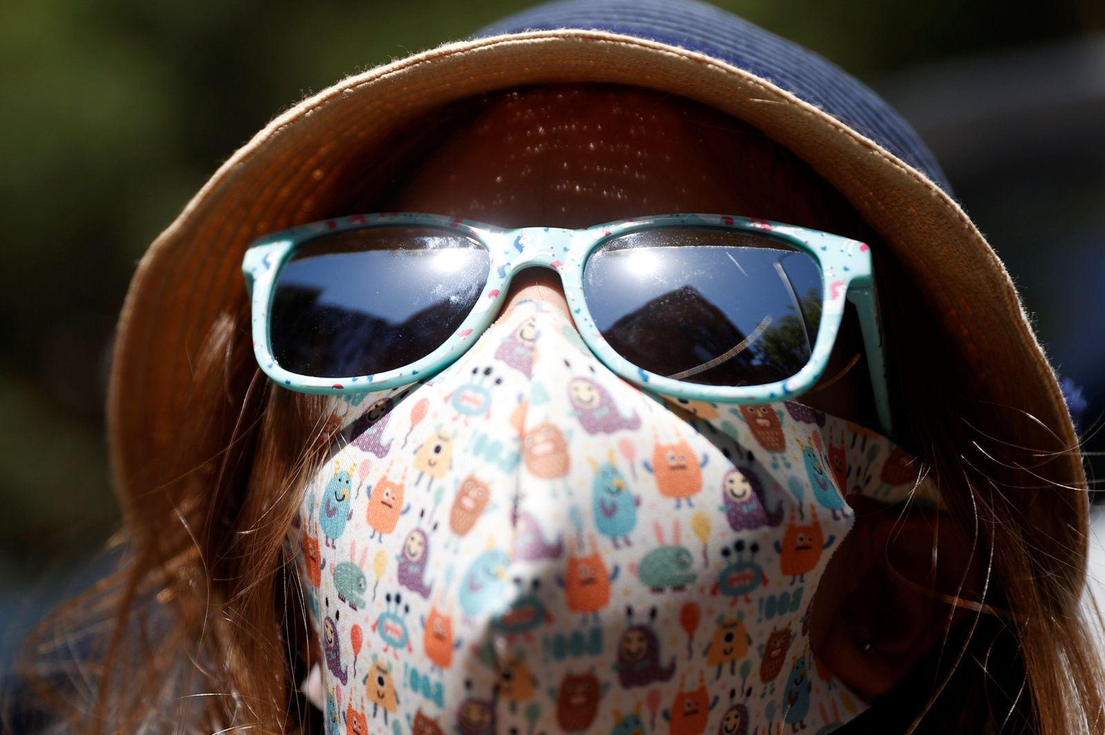 Una niña con mascarilla y sombrero para protegerse del calor.