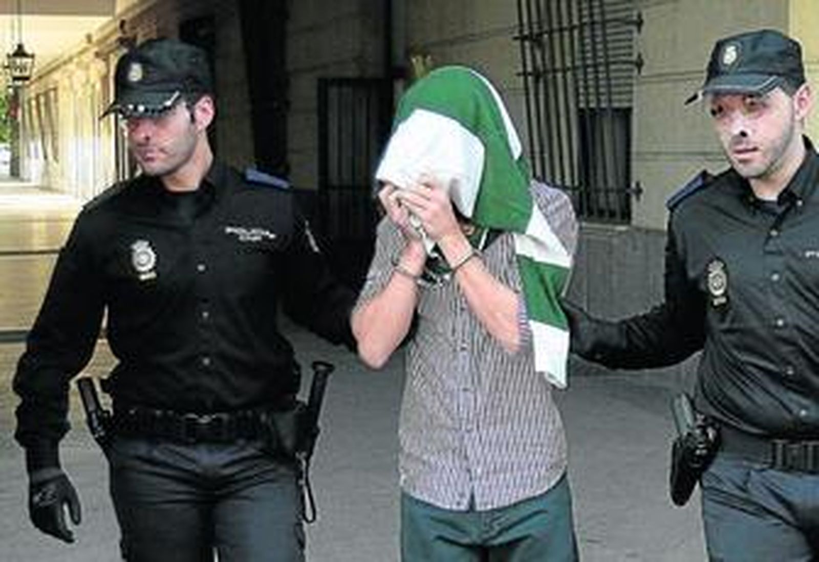 El doble homicida de Tablada sale de los juzgados protegiéndose el rostro con un chaleco y esposado.