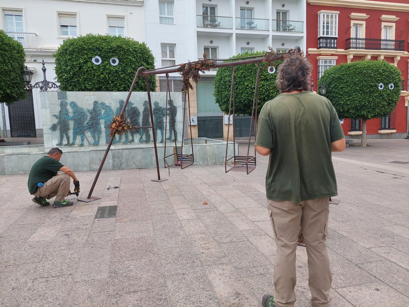 Dos operarios instalan un siniestro columpio em la plaza de la Iglesia.
