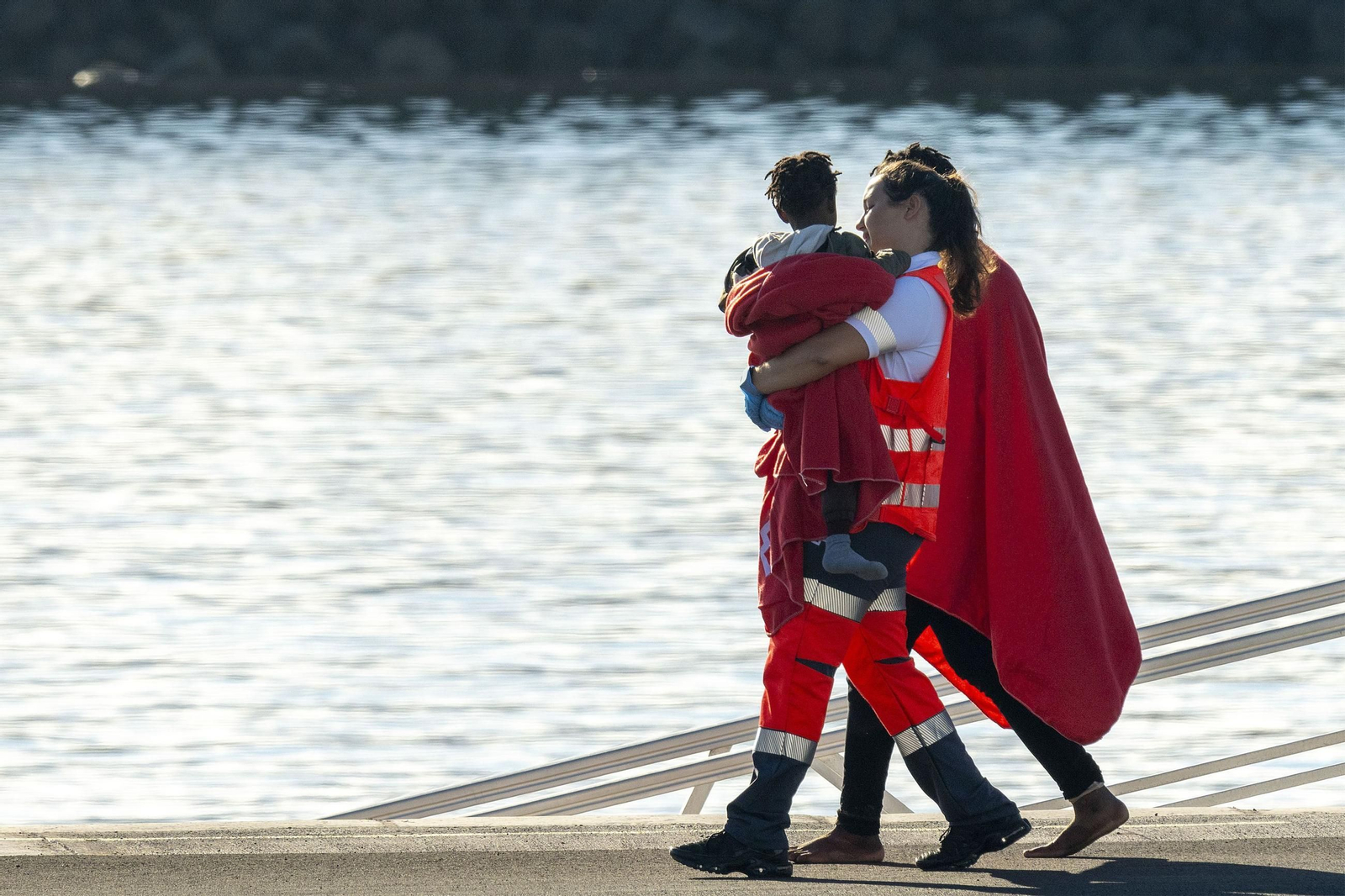 Una trabajadora de la Cruz Roja lleva en brazos a un bebé tras la llegada de una patera a Arrecife.