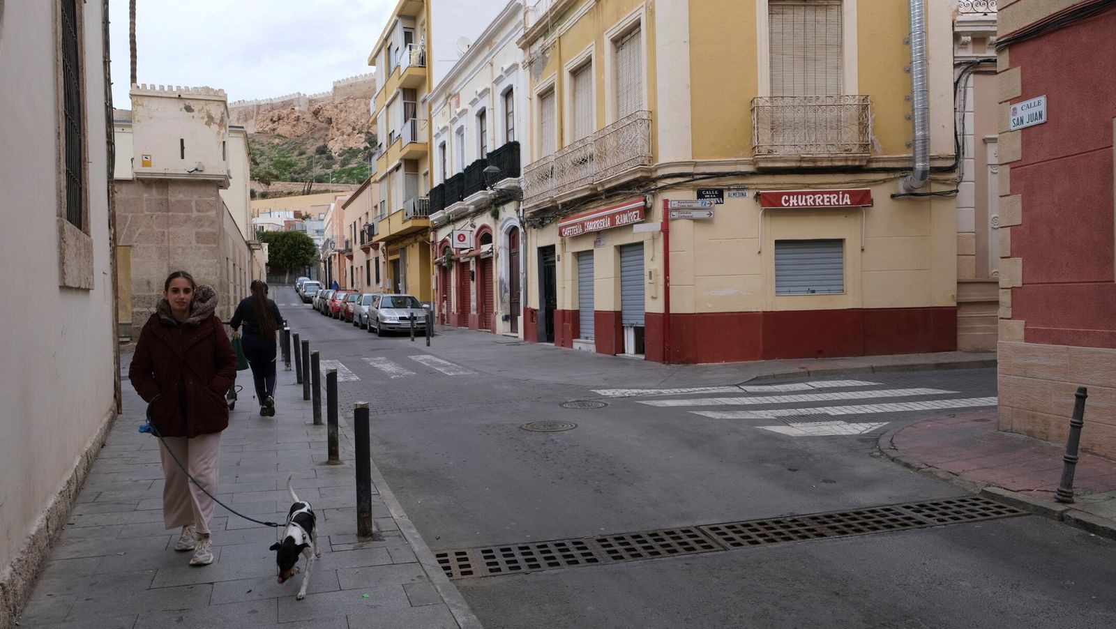 Una joven pasea a su perro en la calle San Juan con las murallas de la Alcazaba de fondo.