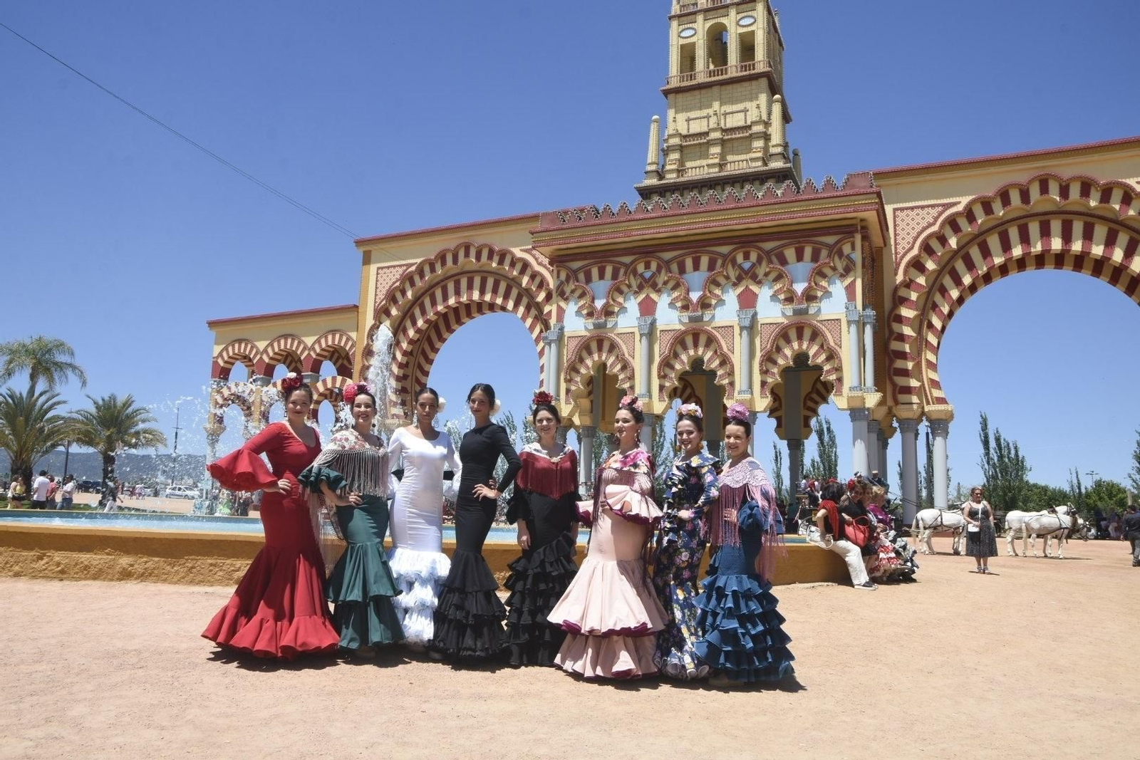 Un grupo de mujeres, vestidas de flamenca, ante la portada de la Feria de Córdoba 2019.