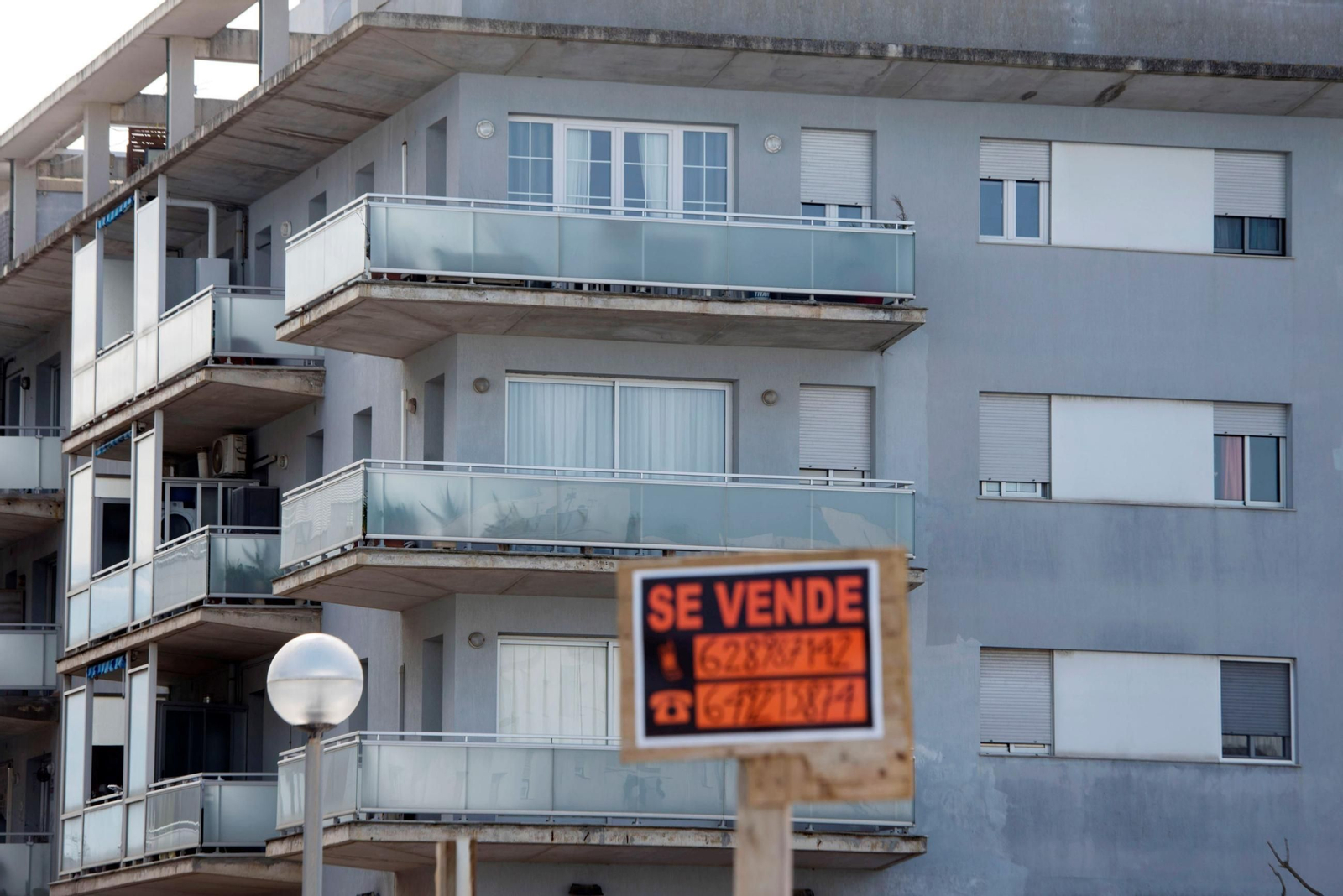 Cartel de venta de vivienda frente a un edificio.