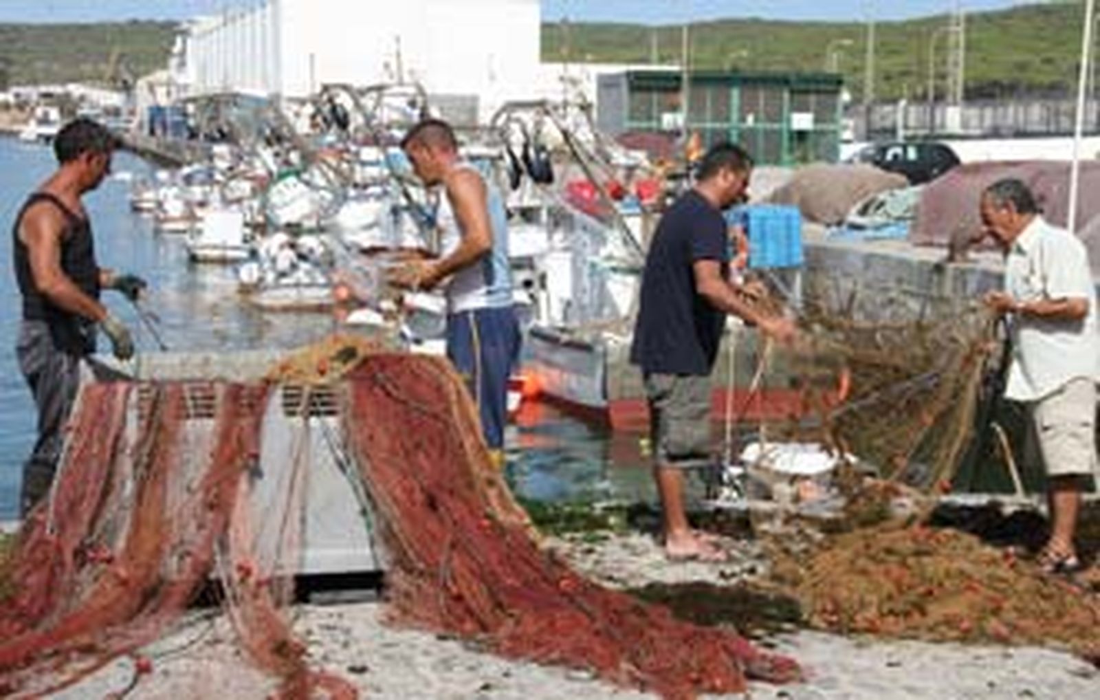 Pescadores de Barbate recogen sus redes con la flota amarrada tras ellos.  Foto: Manuel Aragón Pina