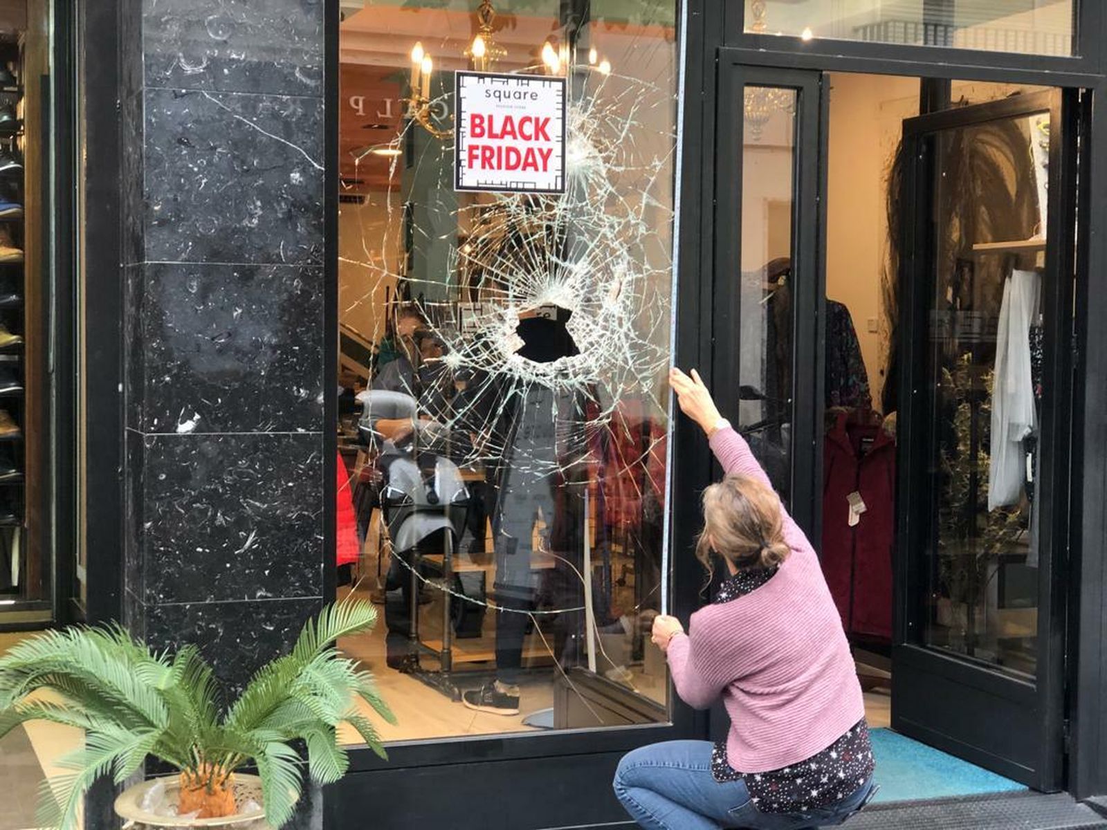 Una mujer toma medidas del cristal, con el agujero hecho por los ladrones.