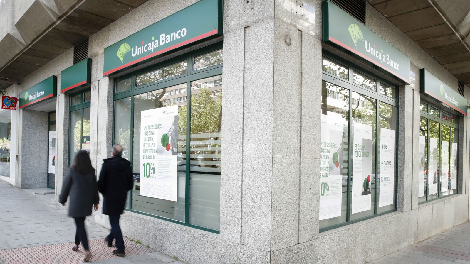 Dos personas pasan junto a una oficina de Unicaja Banco