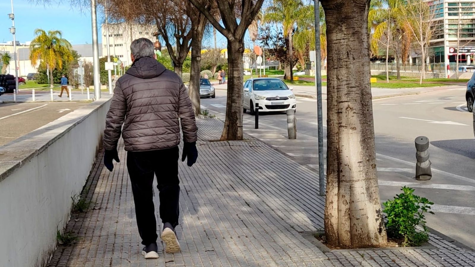 Un hombre con abrigo y guantes pasea por la zona de Hipercor.