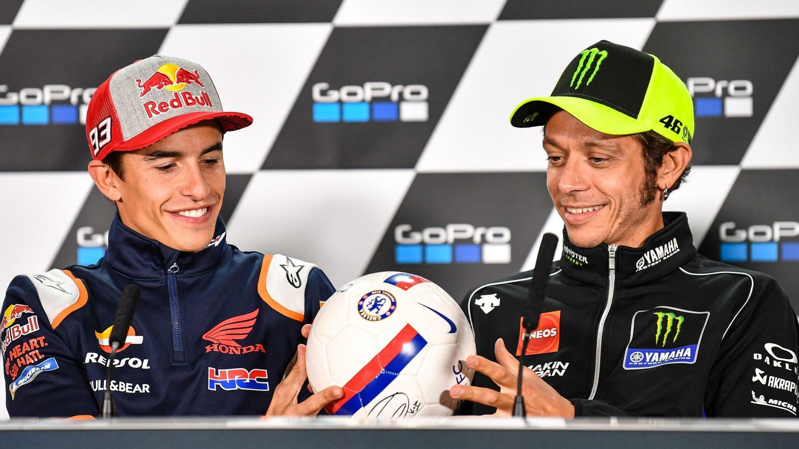 Rossi y Marc Márquez, sonriendo en una rueda de prensa con un balón de fútbol.